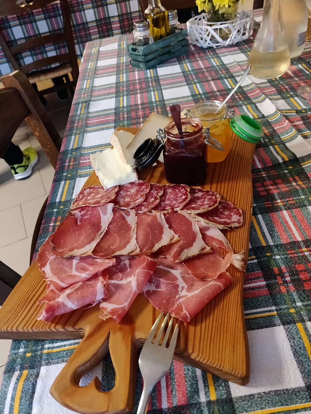 Tagliere di salumi e formaggi con vasetti di miele, servito su un'asse di legno